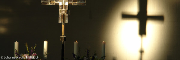 Ein Altarkreuz im Dunkeln, das einen Schatten an die Wand wirft