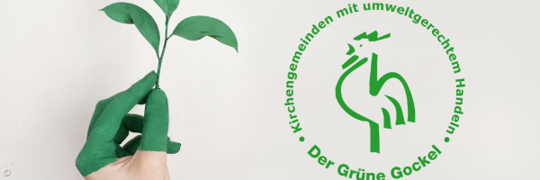 Eine Hand mit grüner Farbe beschmiert hält einen dreiblättrigen Zweig, daneben das Logo vom Grünen Gockel