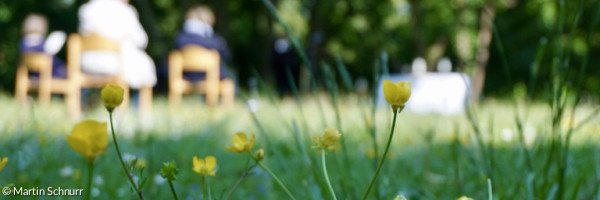 Menschen sitzen zum Gottesdienst auf einer Blumenwiese