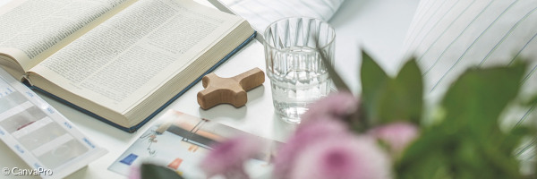 ein Buch, eine Blume und ein kleines Holzkreuz an einem Krankenbett