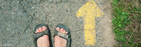 Füße in Sandalen, daneben ein gelber Pfeil, der nach vorne den Weg anzeigt