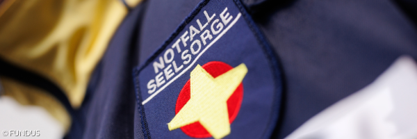 Schulterabzeichen einer Notfallseelsorgerin mit gelb-rotem Notfallseelsorgekreuz