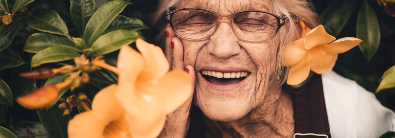 eine ältere Dame steht zwischen orangenen Blumen und lacht