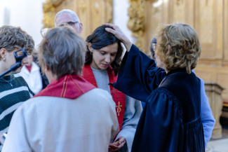 Diakonin Anne Buckel wird von Dekanin Hirschmann gesegnet, weitere Menschen stehen außen herum, Anne Buckel hat ihre Augen geschlossen