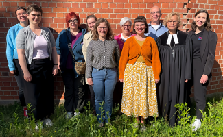 neun Frauen und ein Mann stehen im Gruppenfoto vor einer Ziegelwand