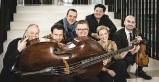 sieben Musikerinnen und Musiker sitzen hinter einem quer liegenden Kontrabass