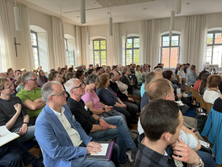Viele Menschen sitzen in Stuhlreihen in einem Saal