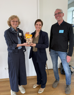 zwei Frauen und ein Mann lächeln, eine Frau überreicht der anderen Frau eine Tüte Nüsse als Geschenk