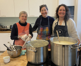 drei Frauen stehen hinter Töpfen in einer Küche und lächeln