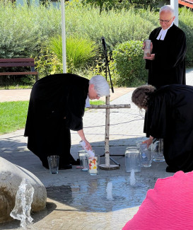 Pfarrerehepaar Wittmann-Schlechtweg und Pfarrerin Schimmel zünden am Brunnen Taufkerzen an