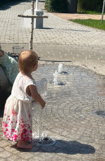 Ein Kleinkind steht barfuß am Wasserspiel im Hallstadter Stadtpark