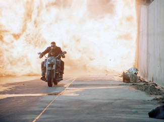 Arnold Schwarzenegger fährt auf einem Motorrad durch eine Feuerwolke