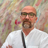 Herr Depner steht mit verschränkten Händen vor einem Bild