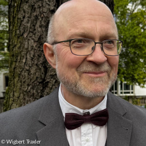 Wigbert Traxler, ein Mann mit Brille, grauem Anzug und Fliege